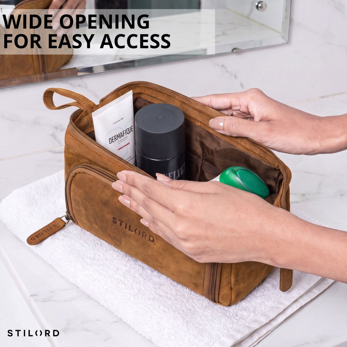 Necessaire em couro na cor tan/marrom escuro, abertura larga com interior visível, mãos organizando produtos, logotipo STILORD